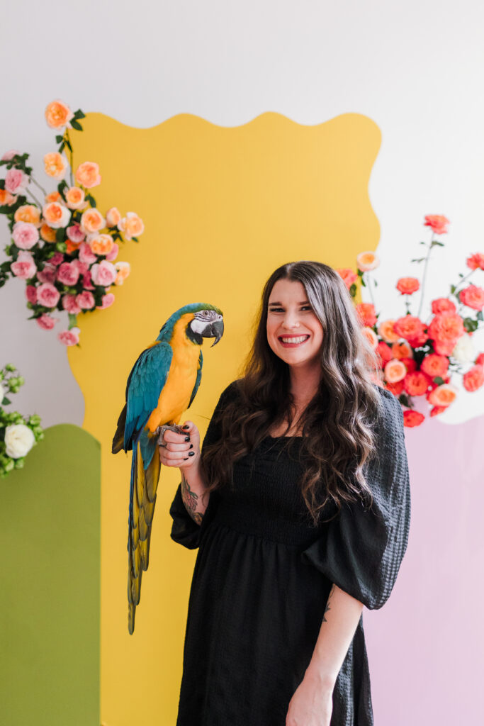 Taylor holding her Parrot, Siren with a background of bright bold flowers